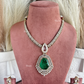 A gold-toned traditional Indian jewelry set displayed on a dusty rose velvet mannequin bust, featuring a necklace with a large green teardrop pendant, matching drop earrings, and a necklace stand.