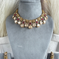 A gold-toned traditional Indian statement necklace with matching drop earrings, displayed on a gray velvet jewelry bust. The necklace features cream-colored stones, red stones, and gold-toned metal details.