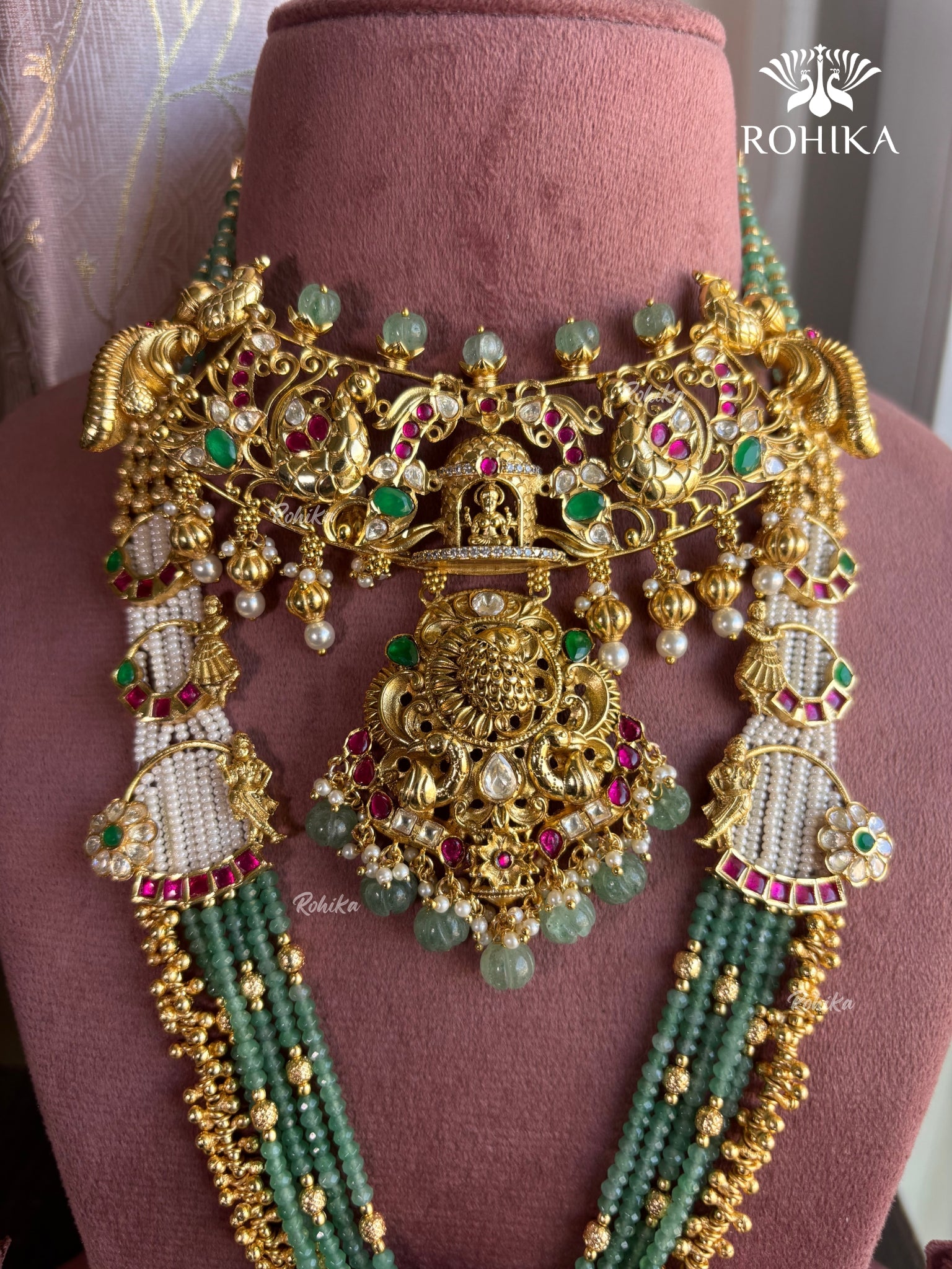 Ornate gold and green necklace on a mannequin with 'Rohika' branding.