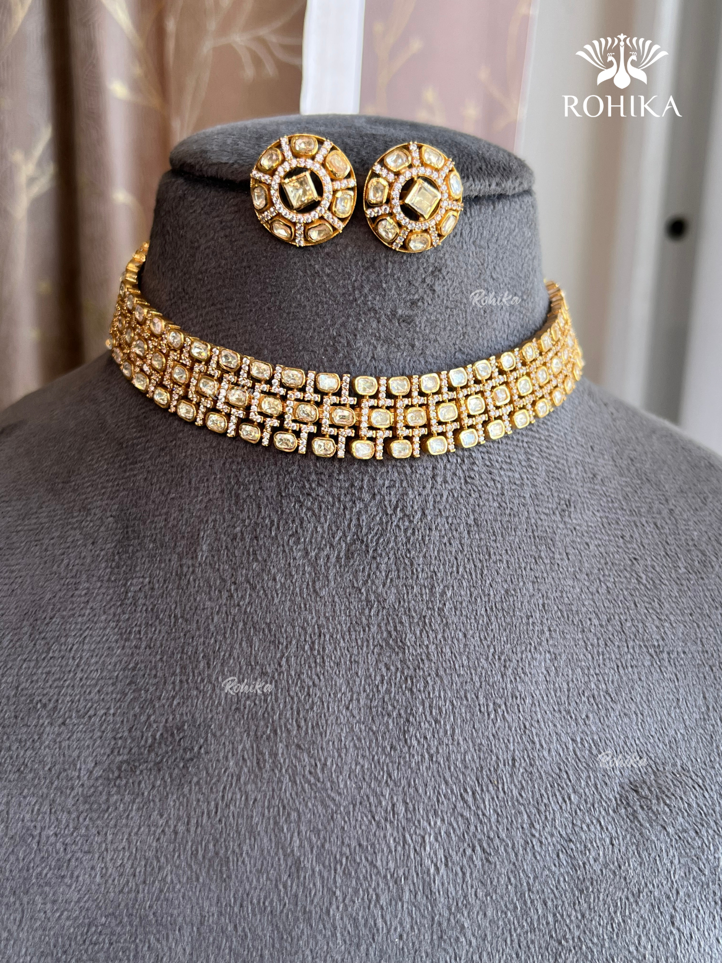 Gold necklace and earrings on a mannequin with 'ROHIKA' branding.